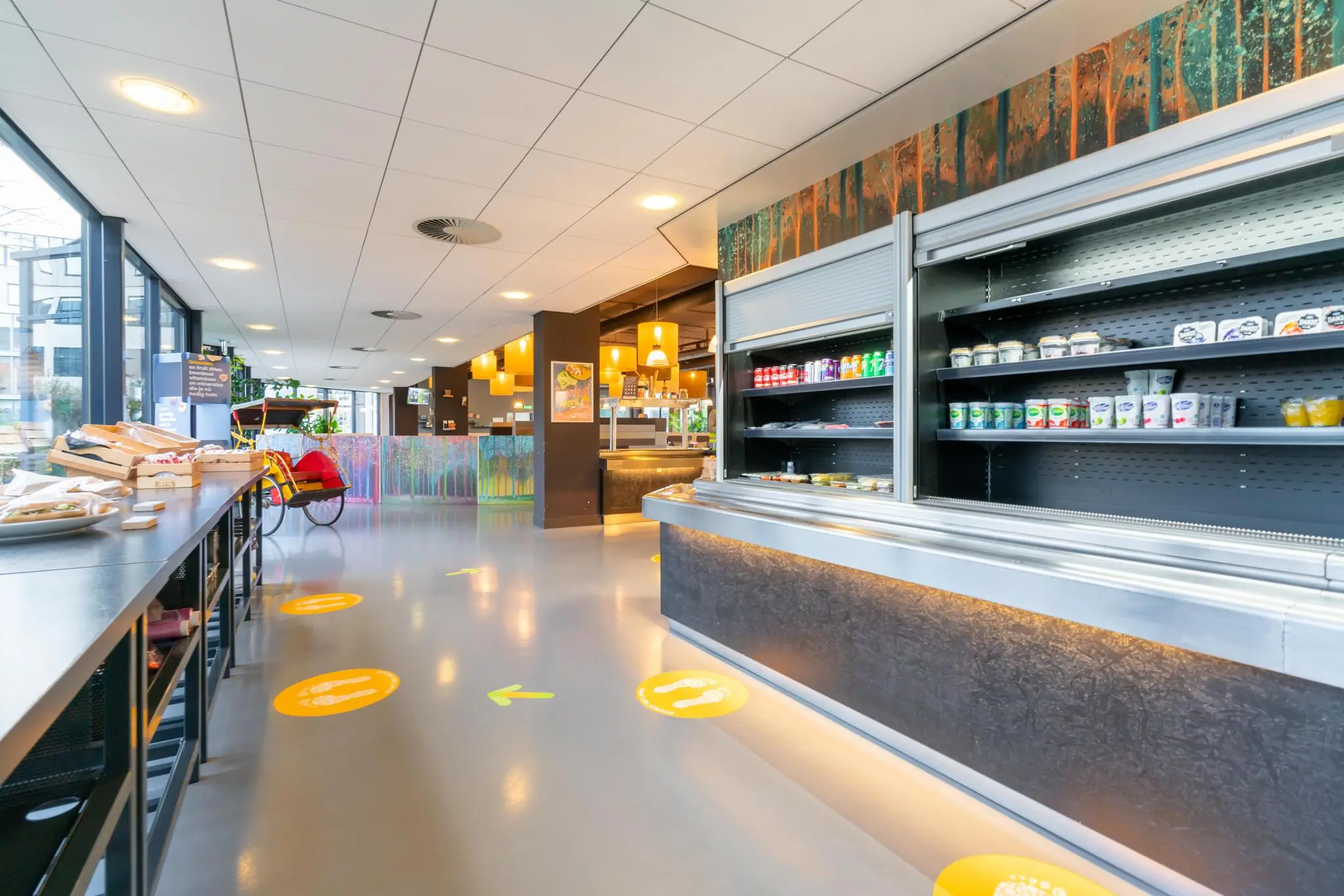 Moderne en kleurrijke bedrijfskantine aan de De Bruyn Kopsstraat met zelfbedieningsrekken en zitgelegenheid.